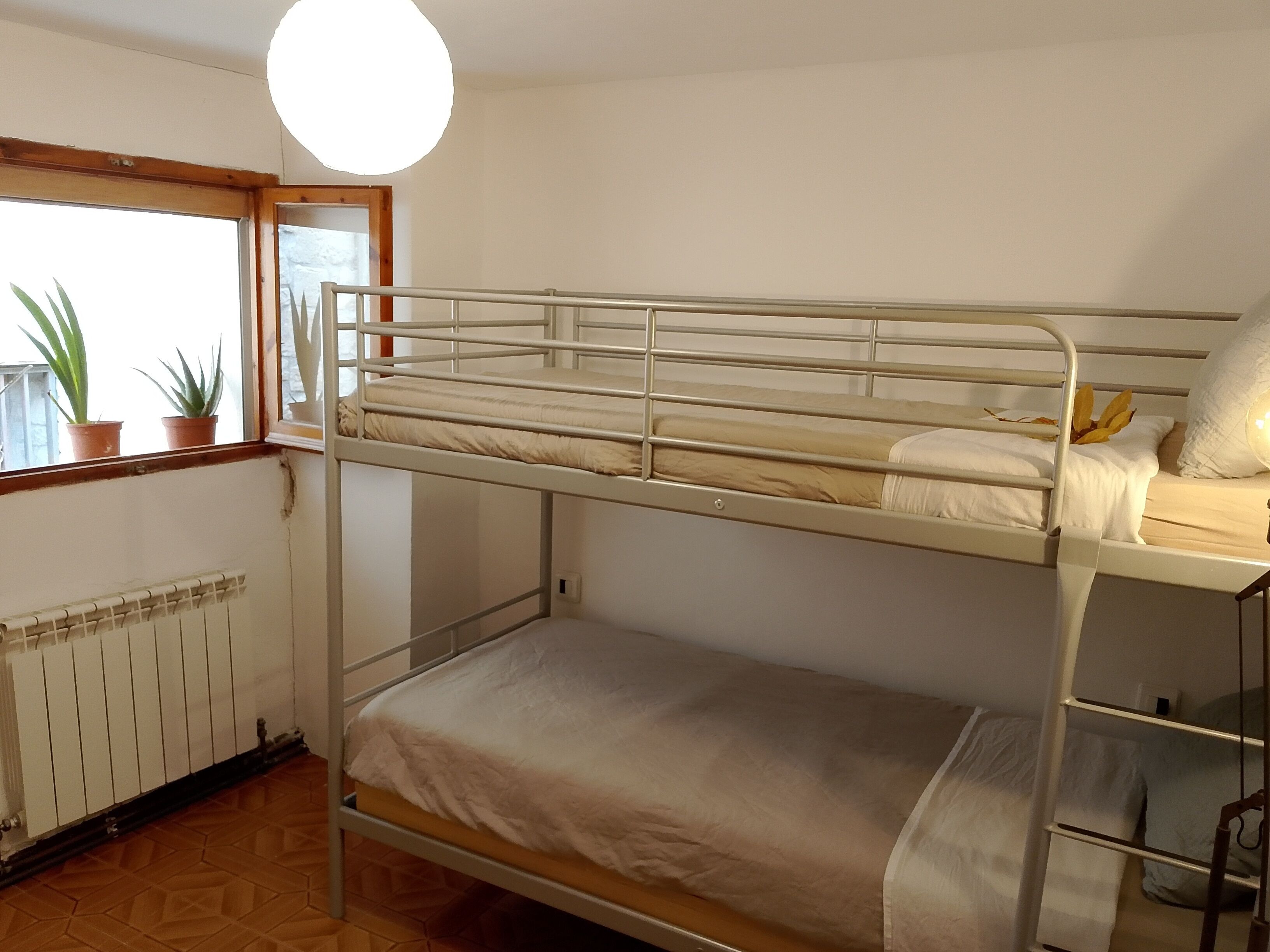 A bunk bed room with a window, radiator, and potted plants.
