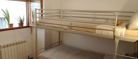 A bunk bed room with a window, radiator, and potted plants.
