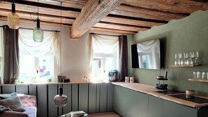 Ein gemütliches Wohnzimmer mit Holzboden, einer Couch, einem Couchtisch und einer Küchenzeile mit Fernseher und Regalen.