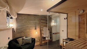 Ein modernes Wohnzimmer mit einem dunklen Sofa, einer Holzleiter und einer Glastrennwand.
