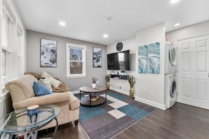 A living room with a sofa, a coffee table, a TV, and a washing machine. - Large 3BR Home Near Dulles w/parking sleeps 8 (Centreville)