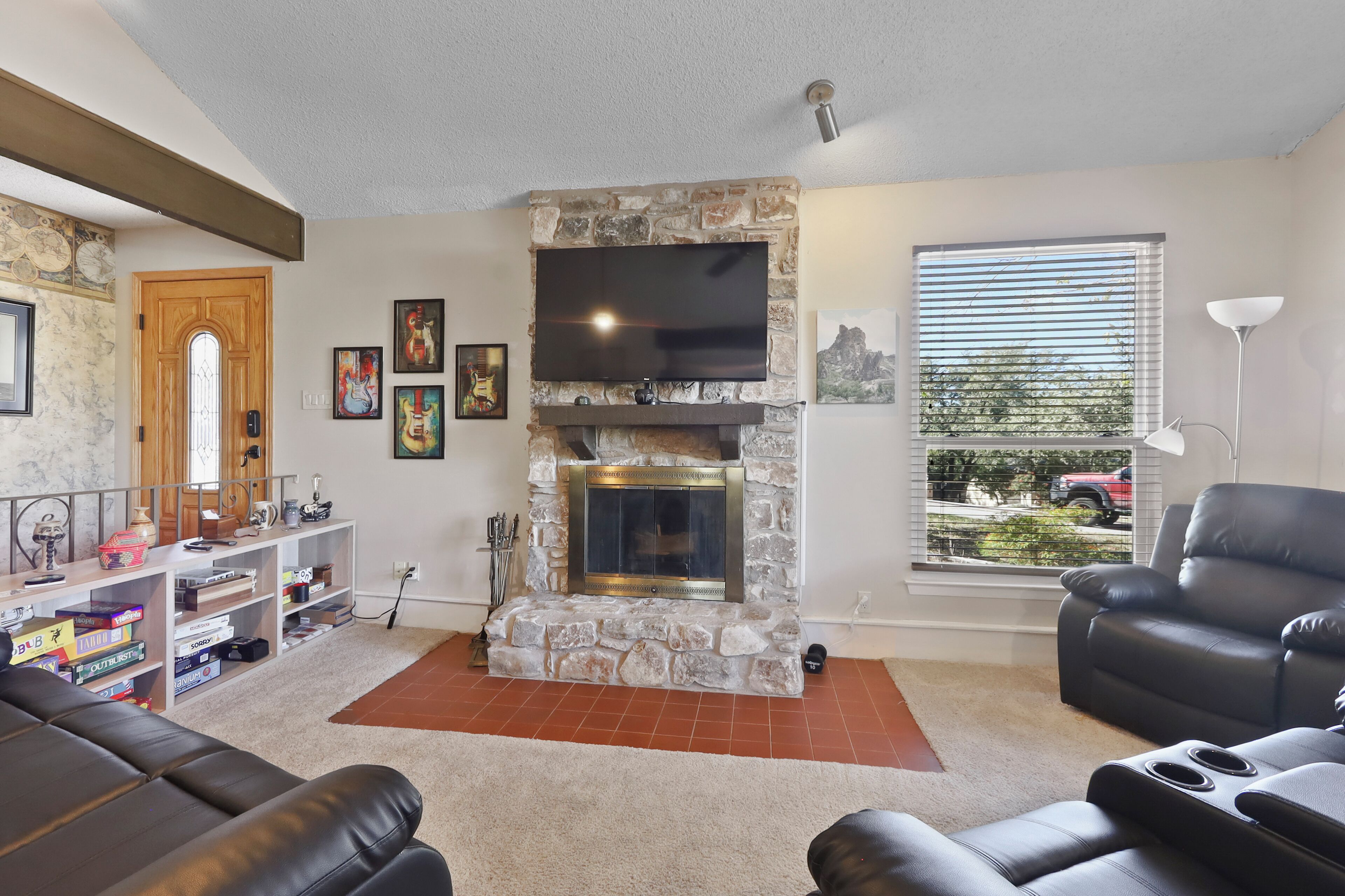 A living room with a stone fireplace, a flat-screen TV, a leather sofa, and a window with blinds.