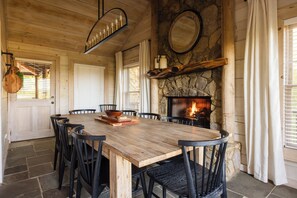 A wooden dining table with chairs, a stone fireplace, and a hanging light fixture. - Whippoorwill Estate - Spa | Mini Golf | B Ball (Mineral Bluff)