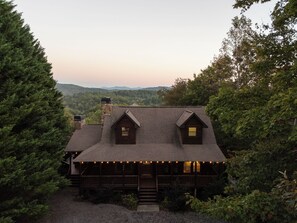A cabin with a steep roof, two dormer windows, and a porch with string lights. - Whippoorwill Estate - Spa | Mini Golf | B Ball (Mineral Bluff)