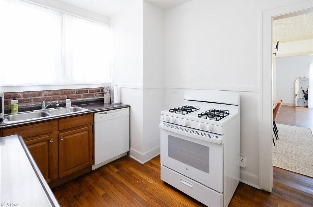 Une cuisine de taille réduite, équipée d’une cuisinière à gaz, d’un lave-vaisselle et de meubles de rangement en bois.