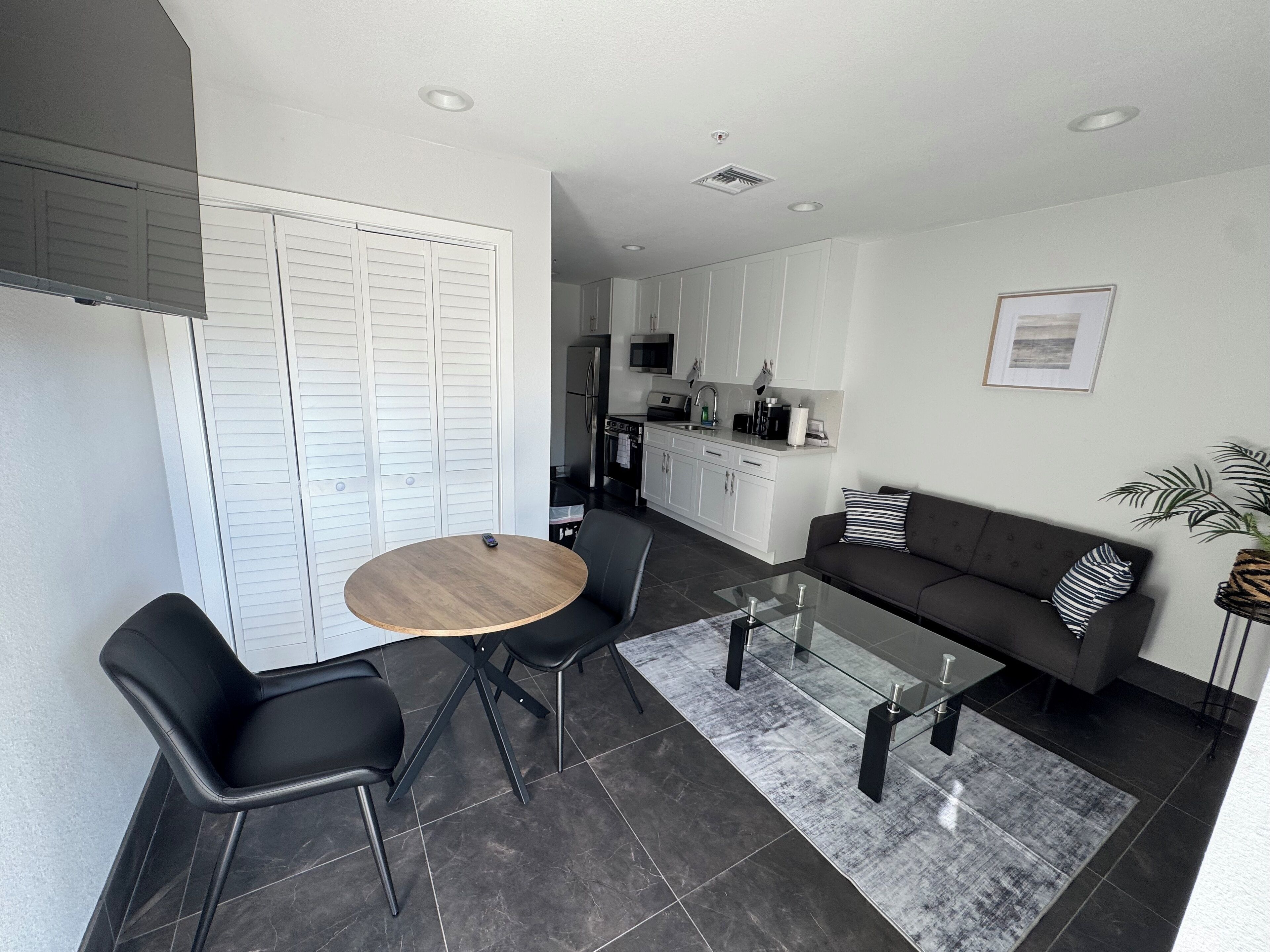 A modern living room with a round table, two chairs, a sofa, and a glass coffee table.