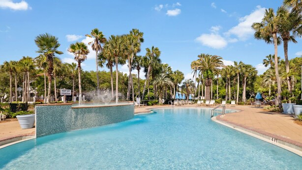 Une piscine aux eaux cristallines, agrémentée d’une fontaine et entourée de palmiers et de chaises longues.