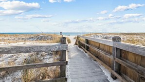 Une promenade en bois qui mène à une plage de sable bordée de dunes.
