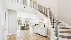 Un vaste espace de vie agrémenté d’un escalier en bois, un coin repas avec une horloge et une vue sur l’extérieur.