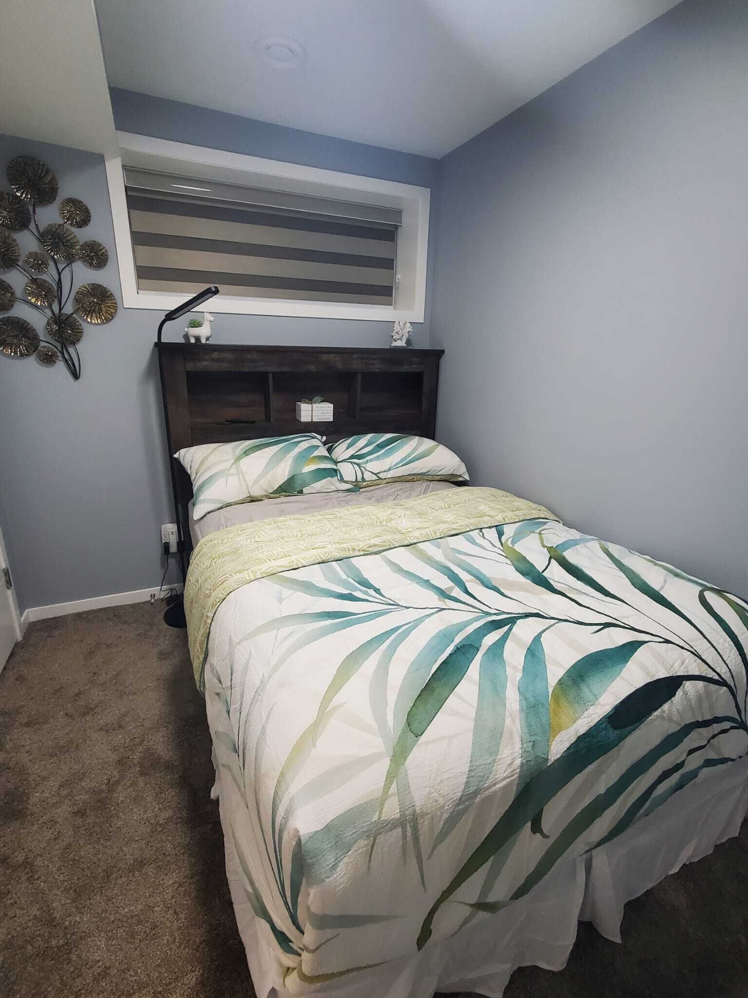Un dormitorio con cama, cabecera, ventana y un adorno en la pared.