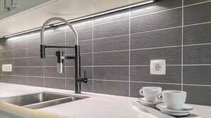 A modern kitchen with a stainless steel sink, a black faucet, and a sleek backsplash. - Cozy apartment in Oostende (Oostende)