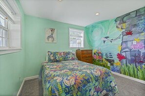 A bedroom with a bed, a dresser, a window, and a mural.