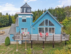 A two-story blue house with a balcony, a small tower-like structure on the roof, and a deck with red chairs. - Coastal Lighthouse Retreat 4mi to Acadia
Sleeps 16 guest (Tremont)