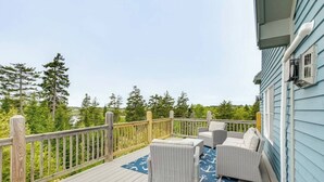 Eine Terrasse mit Korbmöbeln und einem blauen Teppich, mit Blick auf einen bewaldeten Bereich.
