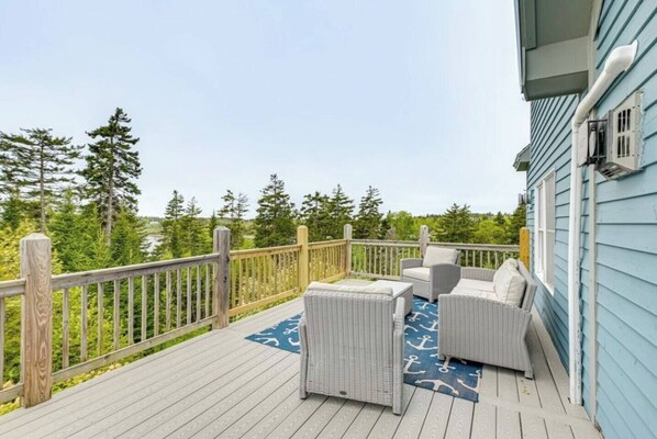 A deck with wicker furniture and a blue rug, overlooking a forested area. - Coastal Lighthouse Retreat 4mi to Acadia
Sleeps 16 guest (Tremont)