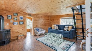 Ein Holzblockhaus-Interieur mit einer Couch, einem Sessel, einem Tisch, einem Kamin und einer Leitern.