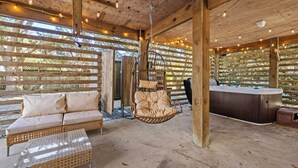 A wooden deck with a hanging chair, a sofa, and a hot tub.