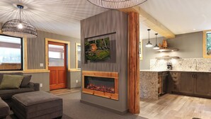 A modern living room with a fireplace, a kitchen with a marble countertop, and a dining area with a wooden table and chairs. - Wintergreen Lodge - D - Hot tub! (Comox-Strathcona C)