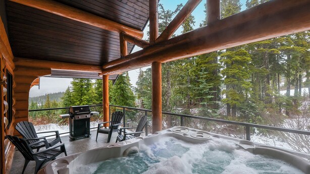 A hot tub with a wooden deck and chairs, overlooking a forested area. - Wintergreen Lodge, Mount Washington - Hot Tub (Comox-Strathcona C)