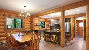 A log cabin interior with a dining area, kitchen, and bar. - Wintergreen Lodge, Mount Washington - Hot Tub (Comox-Strathcona C)
