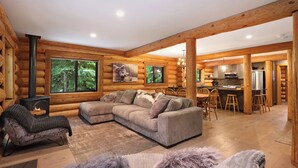 A log cabin interior with a large sofa, a fireplace, a dining area, and a kitchen. - Wintergreen Lodge, Mount Washington - Hot Tub (Comox-Strathcona C)