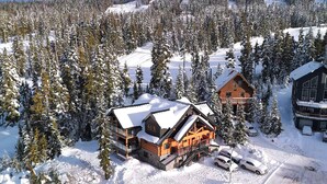 A log cabin with a balcony, surrounded by snow-covered trees and a ski slope. - Wintergreen Lodge, Mount Washington - Hot Tub (Comox-Strathcona C)
