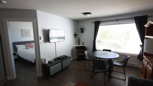 Quarto moderno com cama, escrivaninha, mesa de jantar com cadeiras, televisão e janela com cortinas.