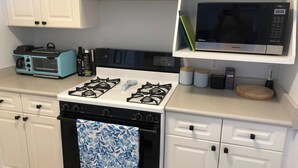 Cozinha equipada com fogão, forno, micro-ondas e torradeira. Há armários, uma prateleira com micro-ondas e uma bancada com torradeira e garrafas.