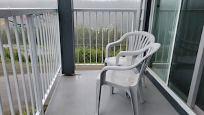A balcony with a white plastic chair, a white railing, and a view of a forested area. - Strathcona Views - Blueberry (Comox-Strathcona C)