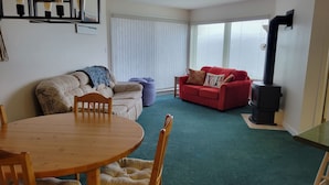 A cozy living room with a round wooden table and chairs, a red sofa with cushions, a beige sofa with a blanket, and a black wood-burning stove. - Strathcona Views - Blueberry (Comox-Strathcona C)