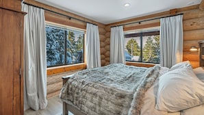 Une chambre dans un chalet en rondins, avec un lit, des rideaux et une vue sur des arbres couverts de neige.