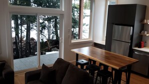 Una cocina moderna con una isla grande, lavavajillas y refrigerador. Hay una puerta corrediza de vidrio que da a una terraza con vista a árboles.