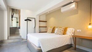 Een moderne slaapkamer met een groot bed, een houten nachtkastje, een wandairconditioner en een trap naar een andere kamer.