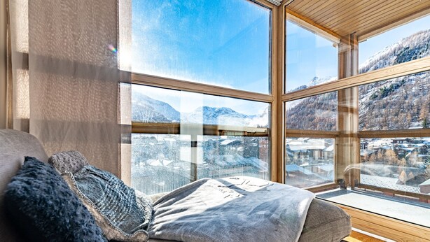 Een gezellige kamer met een groot raam met uitzicht op besneeuwde bergen en een stad daaronder.