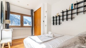Een slaapkamer met een bed, een radiator, een raam met uitzicht op bergen, een houten deur en een zwart boekenrek.