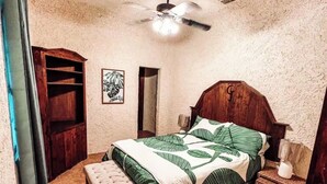 Ein Schlafzimmer mit einem hölzernen Bett, einer Bank, einem Nachttisch, einem Deckenventilator und einem an der Wand befestigten Regal.