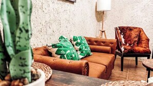 Ein gemütliches Wohnzimmer mit einem braunen Ledersofa, grün gemusterten Kissen, einer Zimmerpflanze und einem gerahmten Kunstwerk an der Wand.