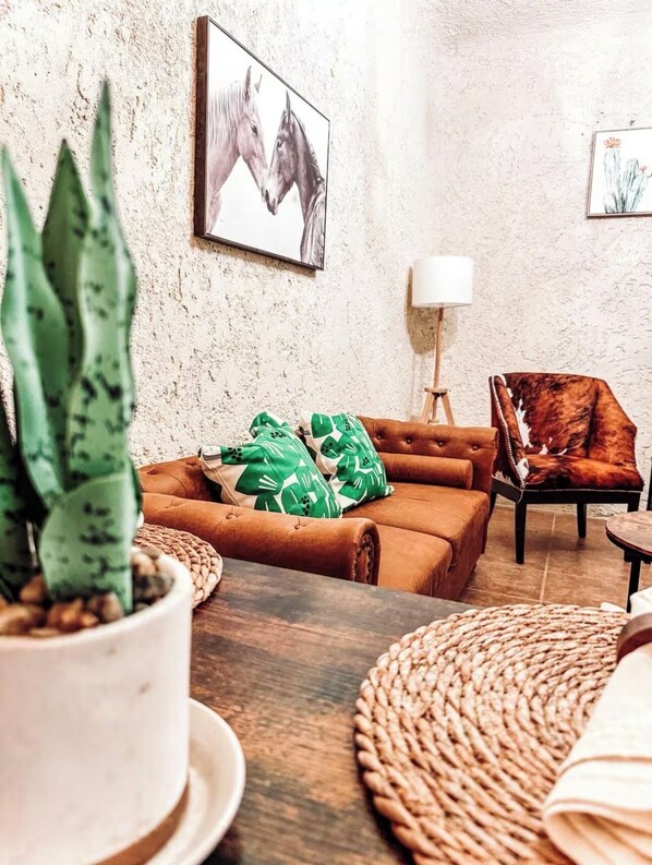 A cozy living room with a brown leather sofa, green patterned pillows, a potted plant, and a framed artwork on the wall. - Charming 1-Bedroom Cottage in Rio Grande City (Rio Grande City)