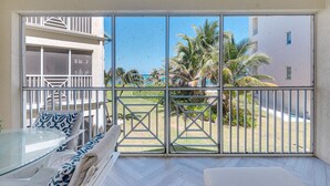 A balcony with a glass table and chairs, a view of palm trees and a building, and a metal gate. - Ocean view 1BR, 1 min to beach, shared pool (Rum Point)