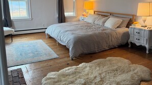 Un dormitorio con cama, mesitas de noche, una alfombra y un manto de piel, además de una ventana con cortinas.