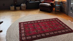 Una habitación acogedora con un ventanal grande, un sillón de cuero, un tapete rojo estampado y una mesita con lámpara.