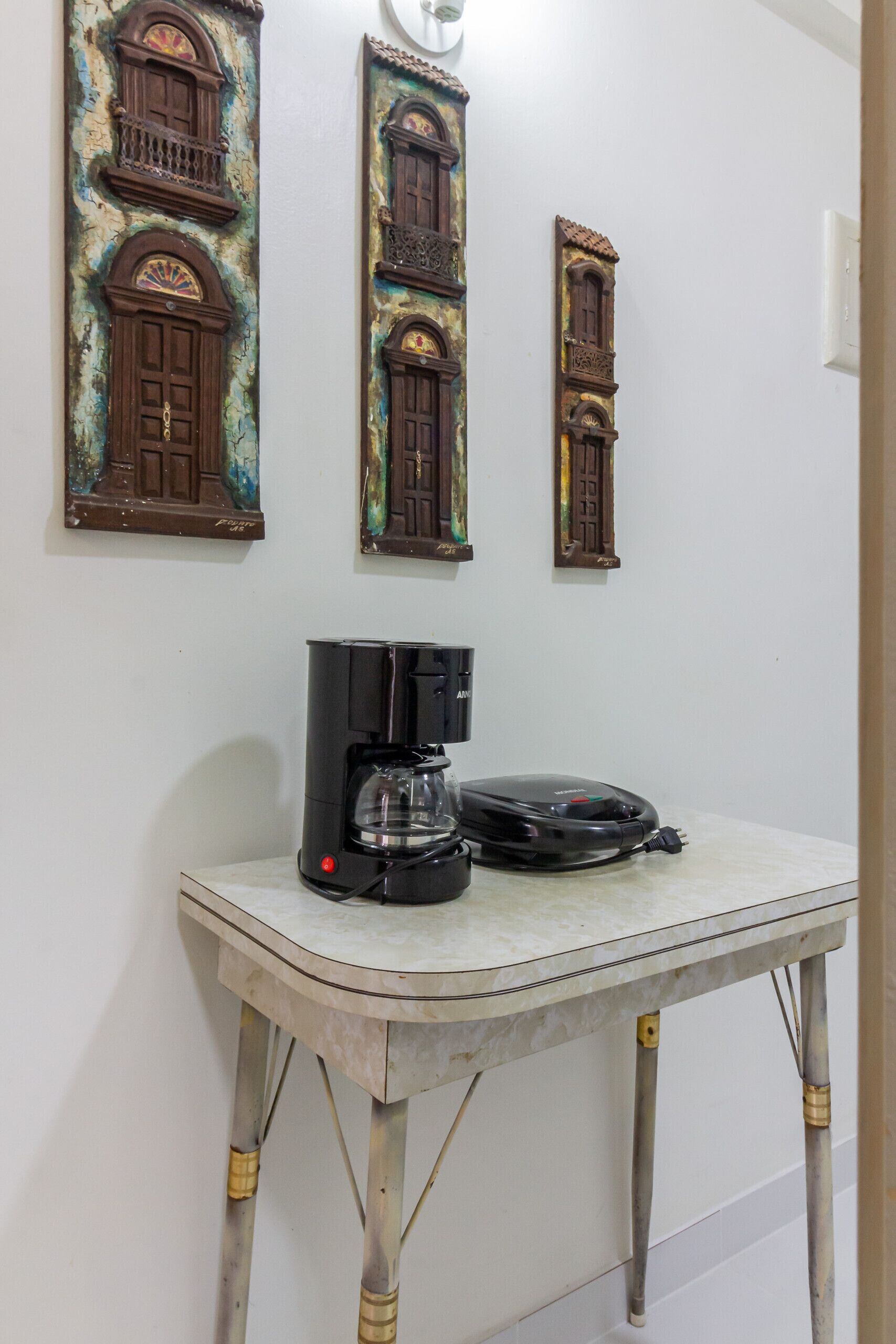 Une table blanche, sur laquelle se trouvent une machine à café et un téléphone noir, est placée devant un mur orné de trois panneaux décoratifs en bois.