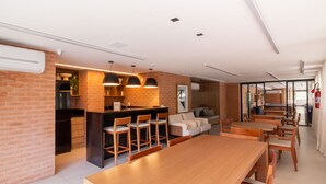 Eine moderne Küche mit Backsteinwand, ein Essbereich mit Holztischen und -stühlen sowie ein Wohnbereich mit Sofa und Couchtisch.