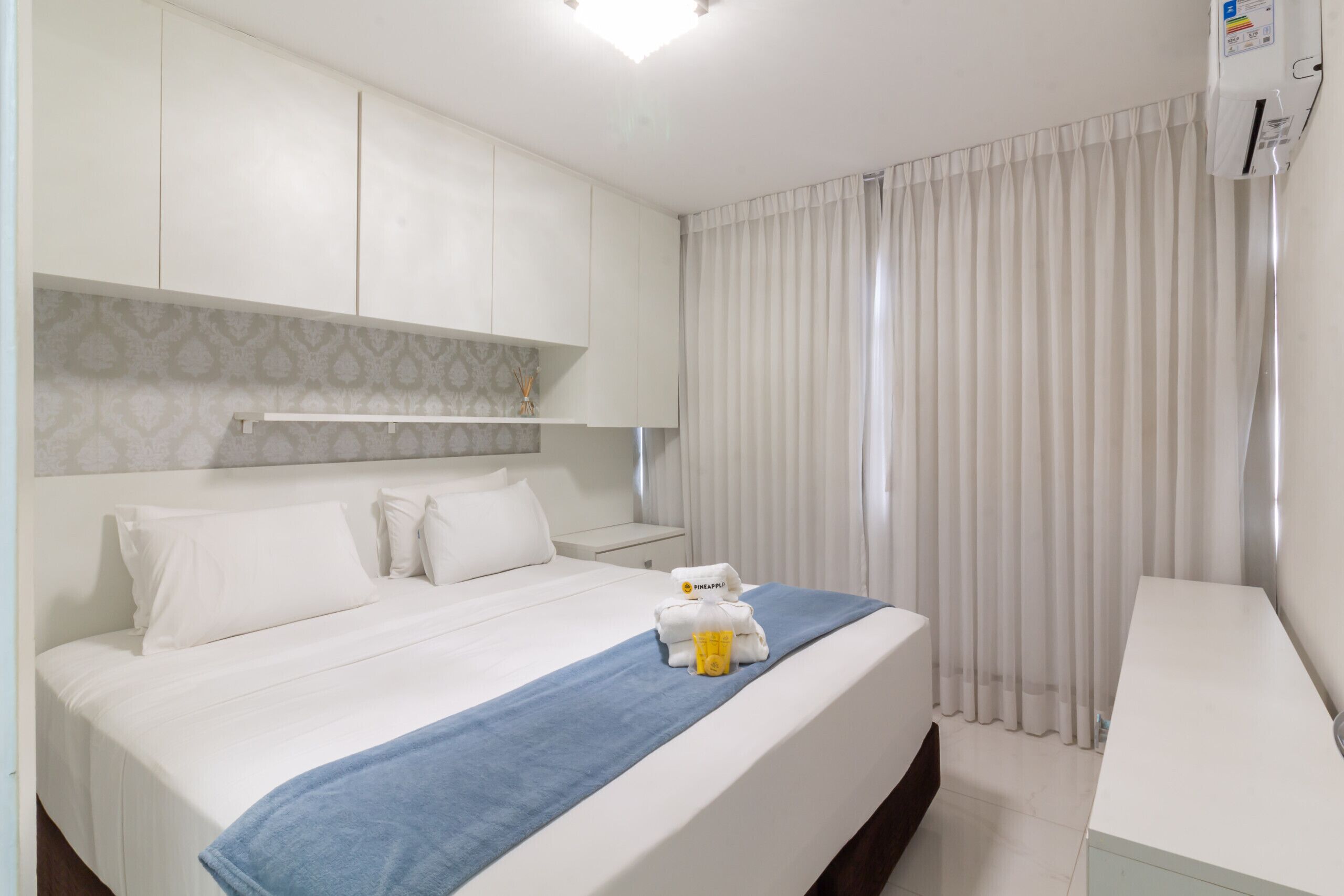 A hotel room with a bed, a desk, a nightstand, and a window with curtains.