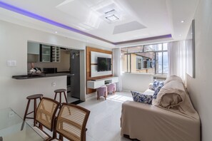 A modern living room with a sofa, a TV, and a kitchen area with a bar. - Acogedor Rincón en Ipanema | AC2002 (Rio de Janeiro)