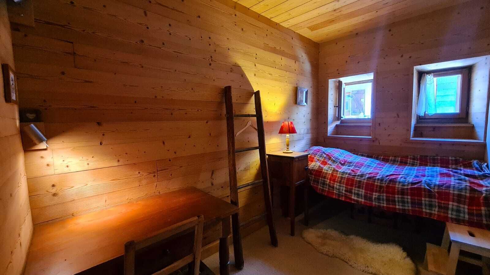 Una camera accogliente in legno, con un letto ricoperto da una coperta a quadri, un tavolino con una lampada e una scala appoggiata al muro.