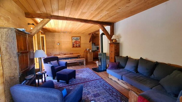 Ein gemütliches Blockhaus-Interieur mit Holzboden, einer Couch, einem Sessel, einem kleinen Tisch und einem Kamin.