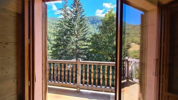 Ein Holzbalkon mit Geländer, mit Blick auf eine bewaldete Berglandschaft.