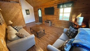 Interno di una baita di legno con divano, poltrona, tavolino e televisore.