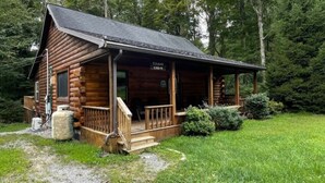 Una baita di legno con un portico, con l'indicazione "Cousar Cabin", immersa in una zona boschiva.